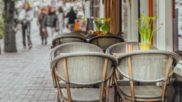 empty tables and chairs standing on a sidewalk outside of a restaurant
