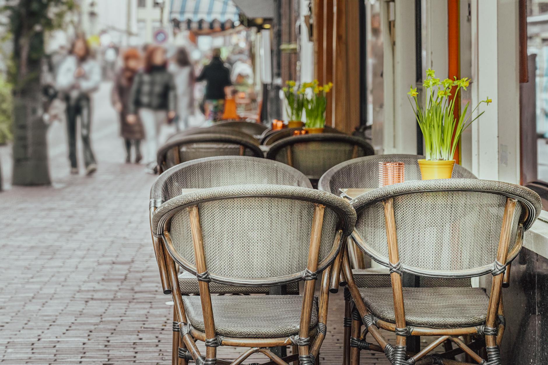 empty tables and chairs standing on a sidewalk outside of a restaurant